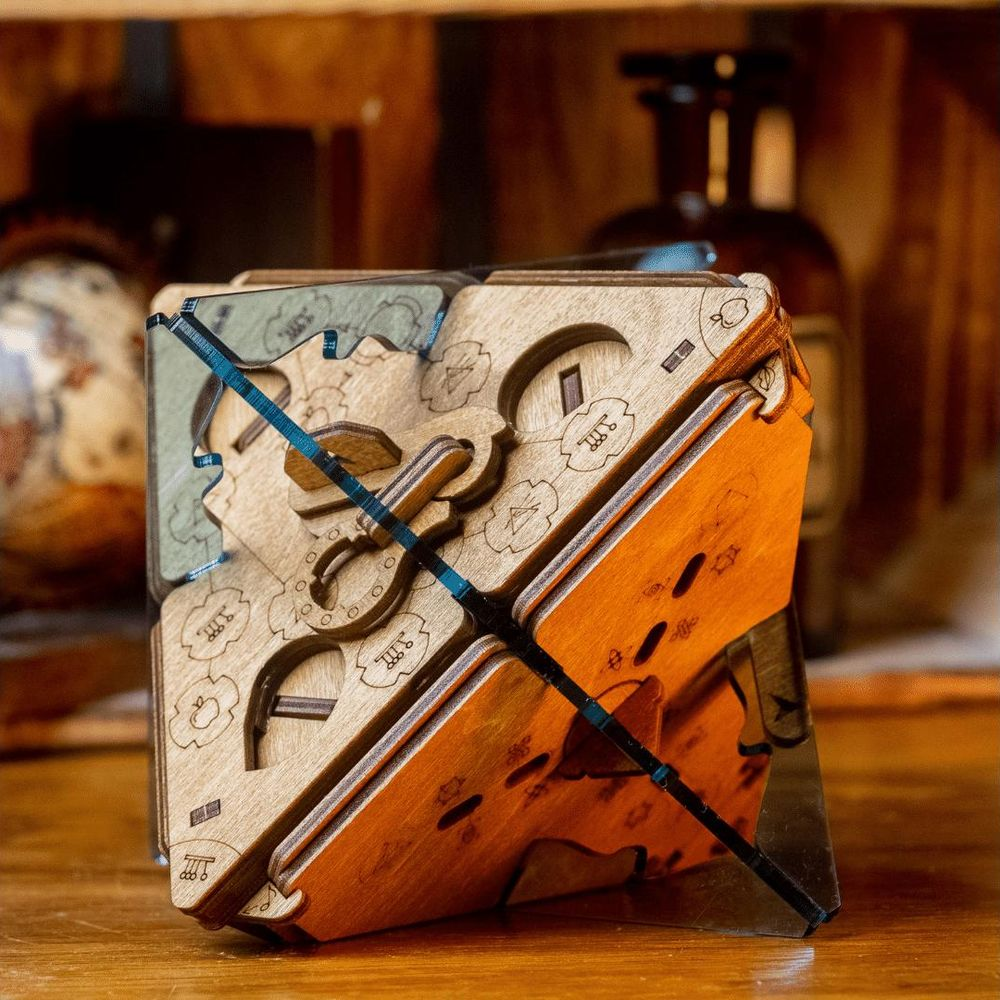 Un cubo puzzle di legno con ingranaggi e simboli incisi si trova su una superficie di legno.