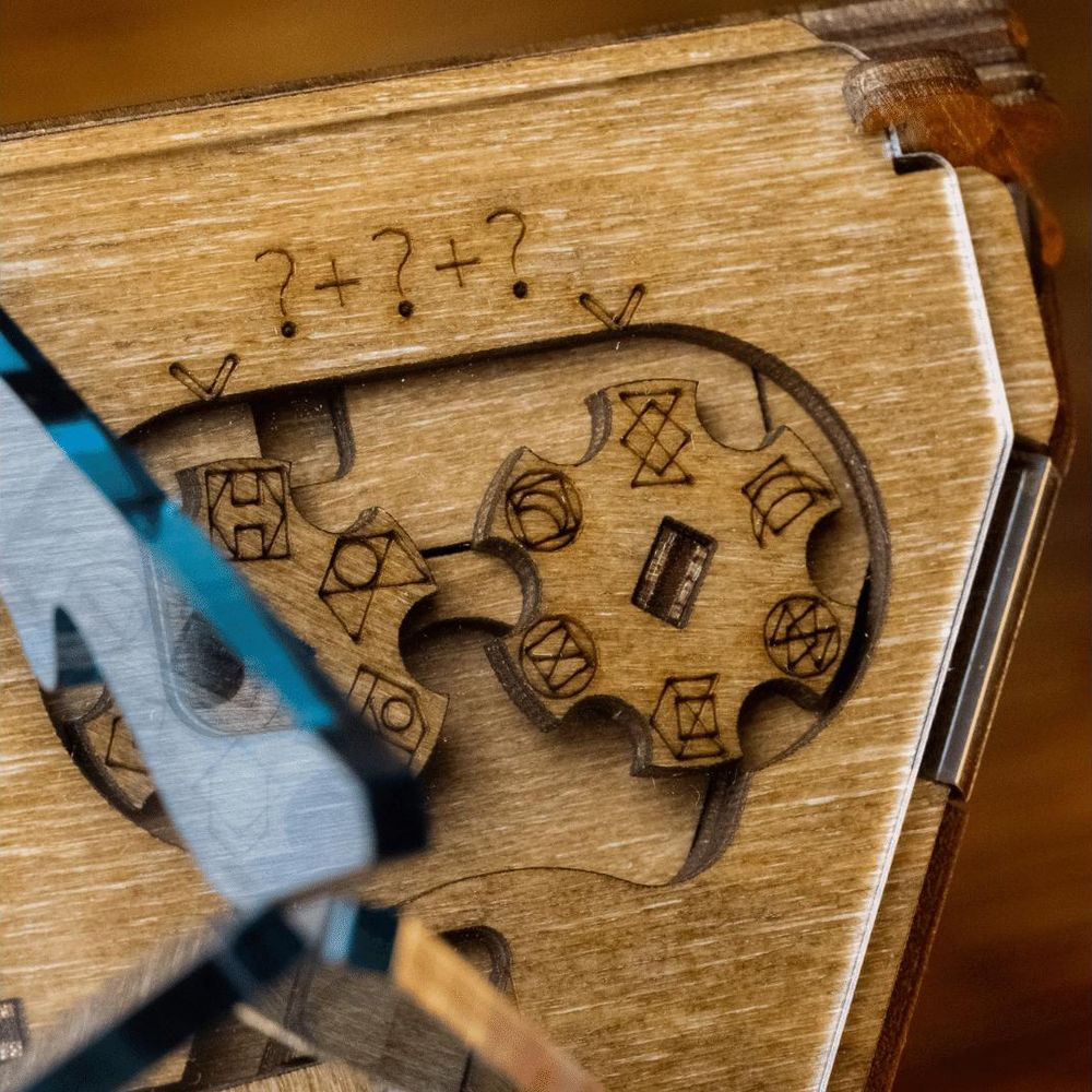 Puzzle box in legno con ingranaggi e simboli. "?+?+?" inciso sopra.
