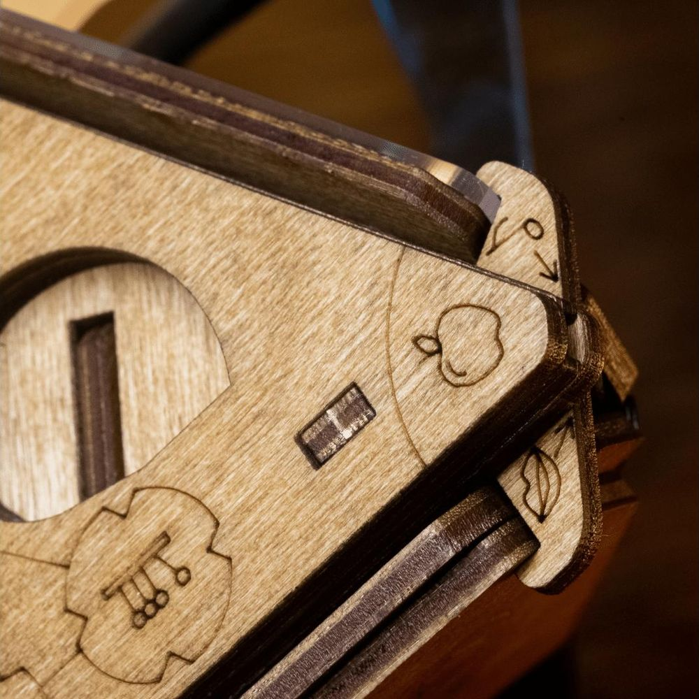 Primo piano di una scatola puzzle in legno con intricati disegni incisi al laser di una mela e ingranaggi.
