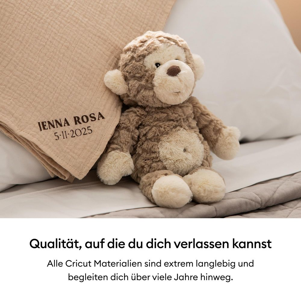 Ein brauner Teddybär sitzt neben einer beigefarbenen Decke mit Namen.