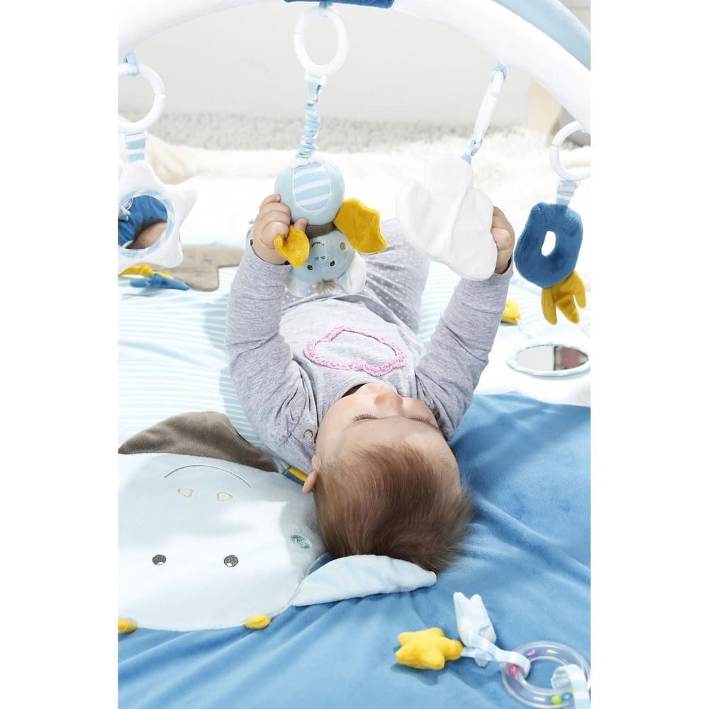 Baby liegt auf dem Rücken und spielt mit Spielzeug an einer Spieldecke mit Elefantenmotiv.