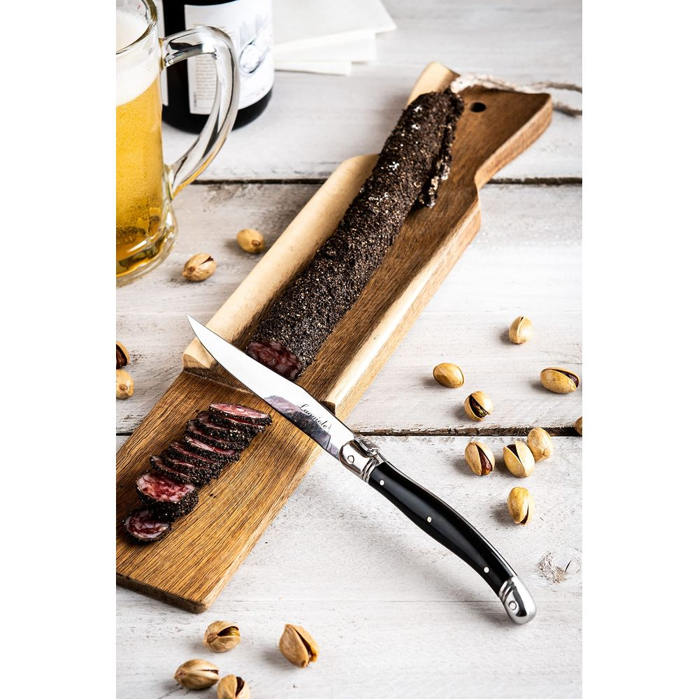 Geräucherte Salami auf einem Holzbrett mit einem Messer, Bier und Pistazien.