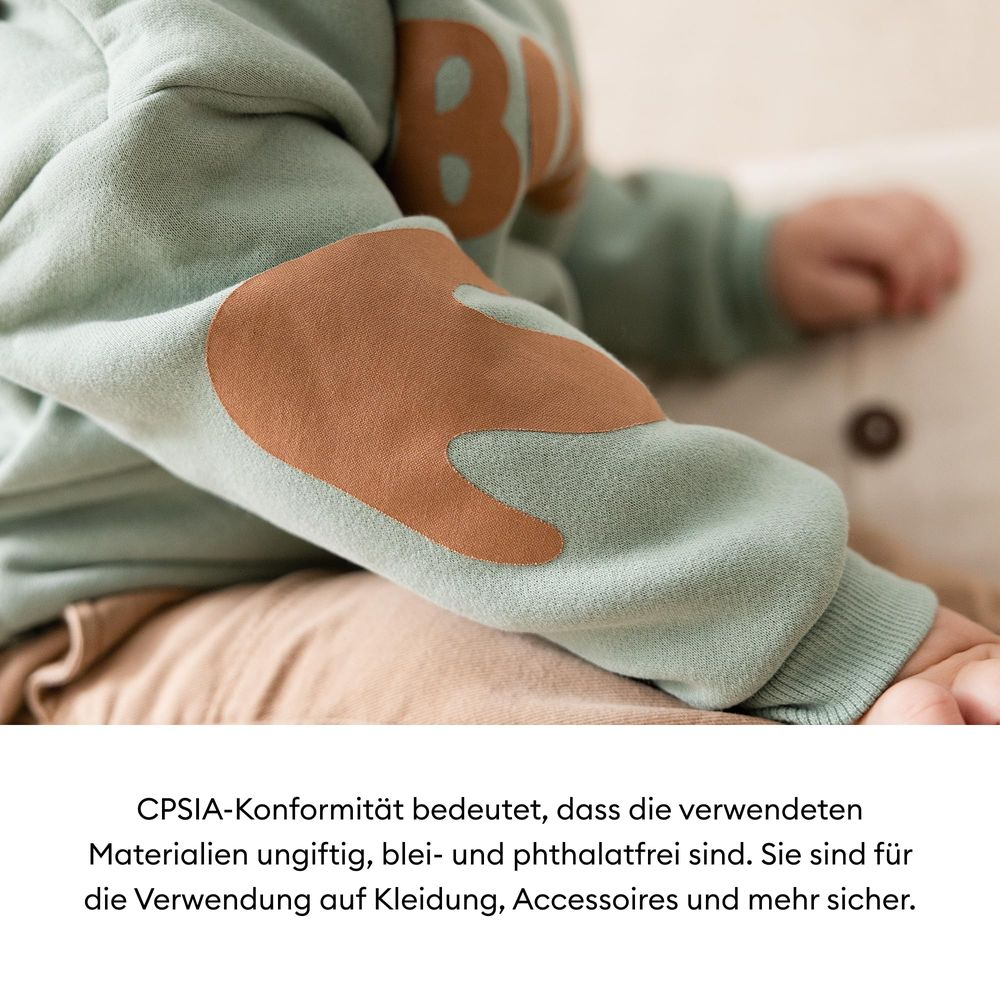 Ein Kind trägt einen hellgrünen Pullover mit braunen Ellbogenflicken.