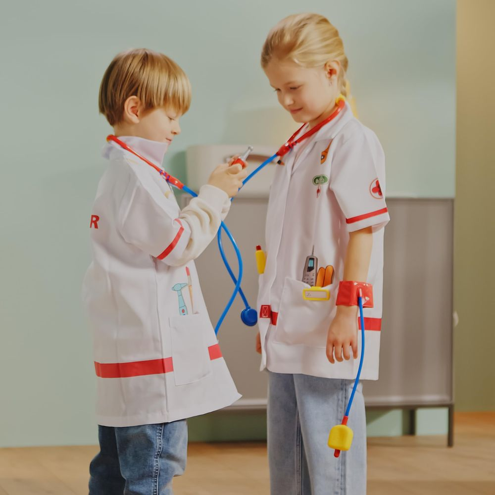 Dos niños con batas de médico juegan con estetoscopios y juguetes.