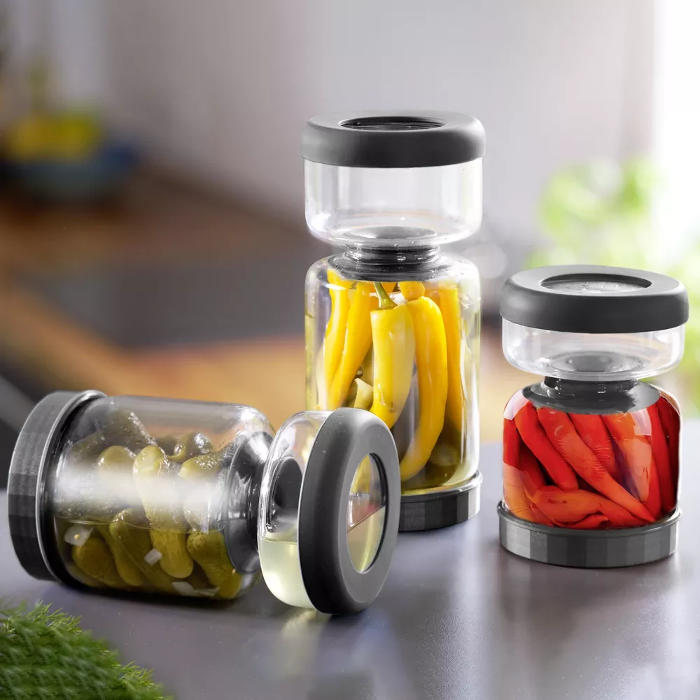 Drei Gläser mit eingelegtem Gemüse: Gurken, gelbe und rote Chilis.
