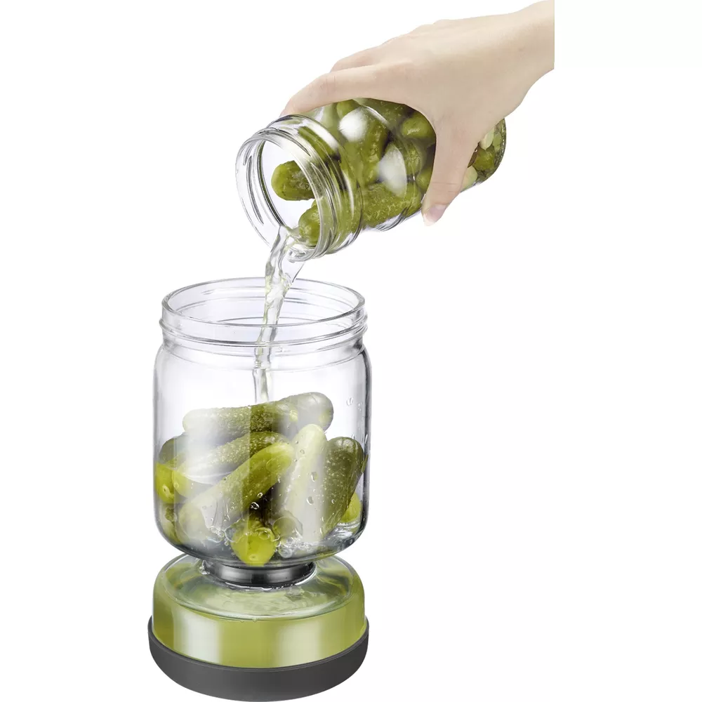 Essiggurken werden aus einem Glas in ein anderes Glas mit grünem Sockel gegossen.