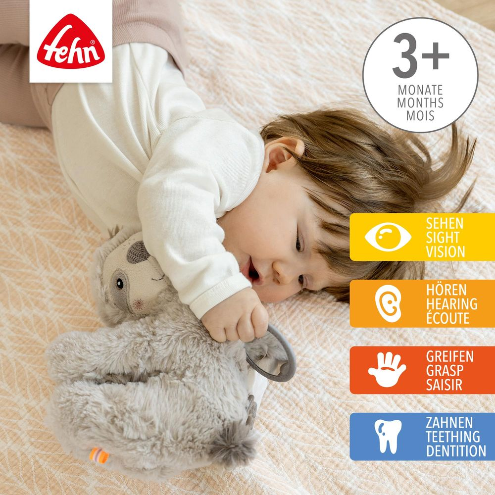 Ein Baby spielt mit einem Plüschtier. Icons zeigen Sehen, Hören, Greifen, Zahnen.