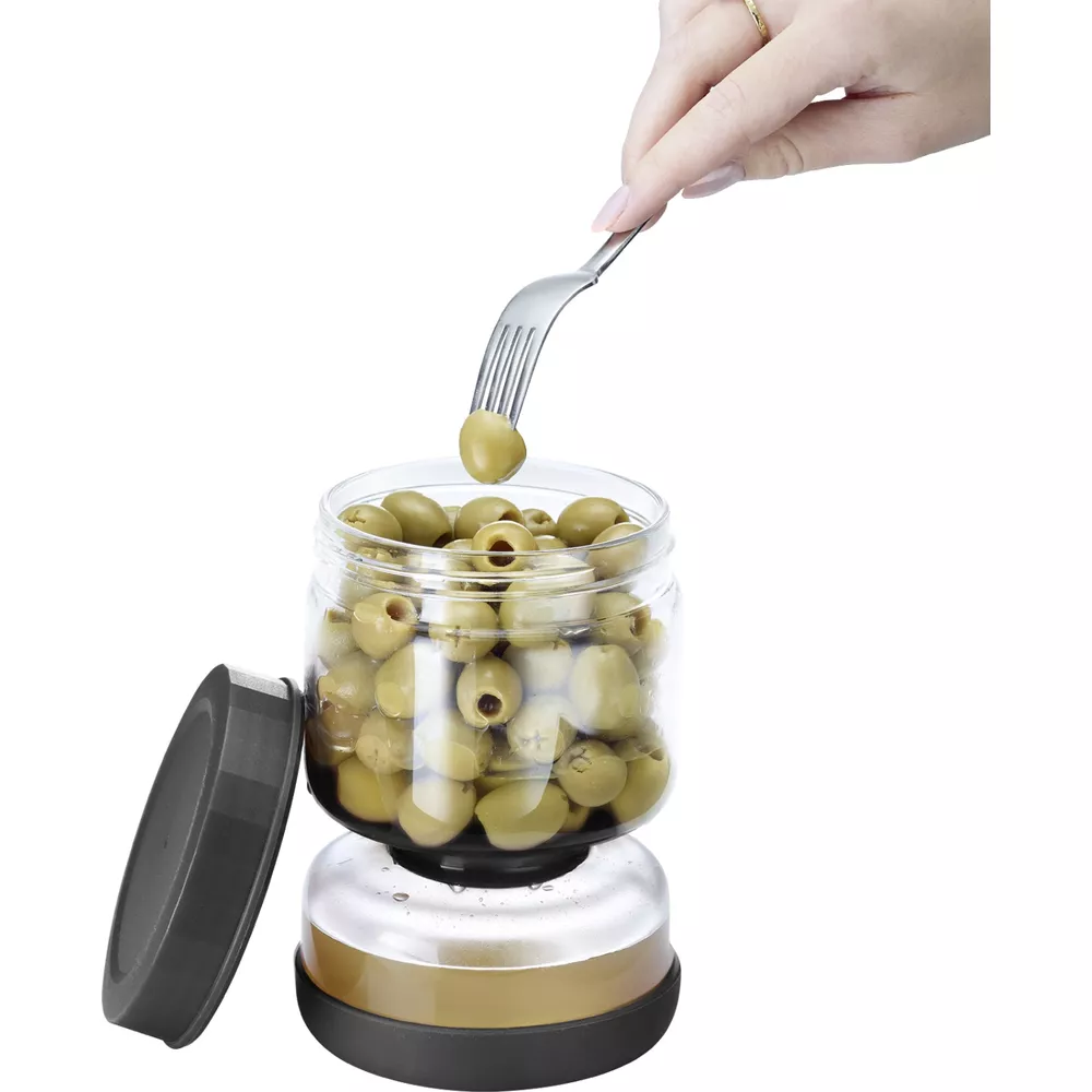 Eine Gabel hebt eine grüne Olive aus einem Glas mit Oliven.