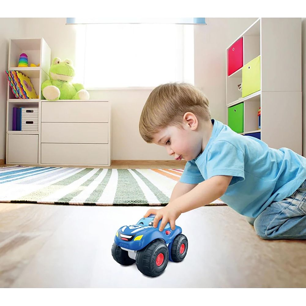 Ein kleiner Junge spielt mit einem blauen Monstertruck-Spielzeug auf dem Boden.