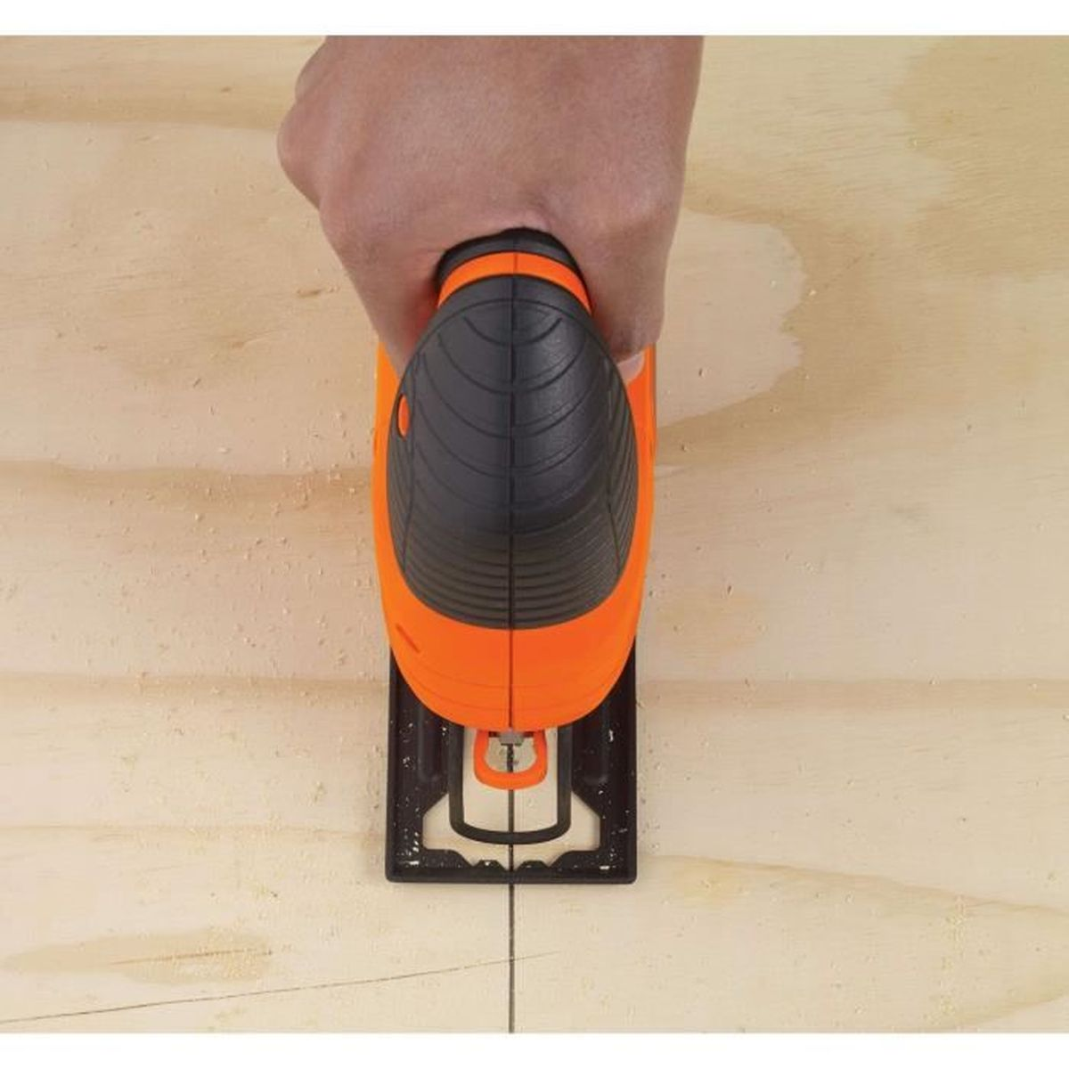 Een hand houdt een oranje en zwarte decoupeerzaag vast die een lijn snijdt op een licht houten oppervlak.