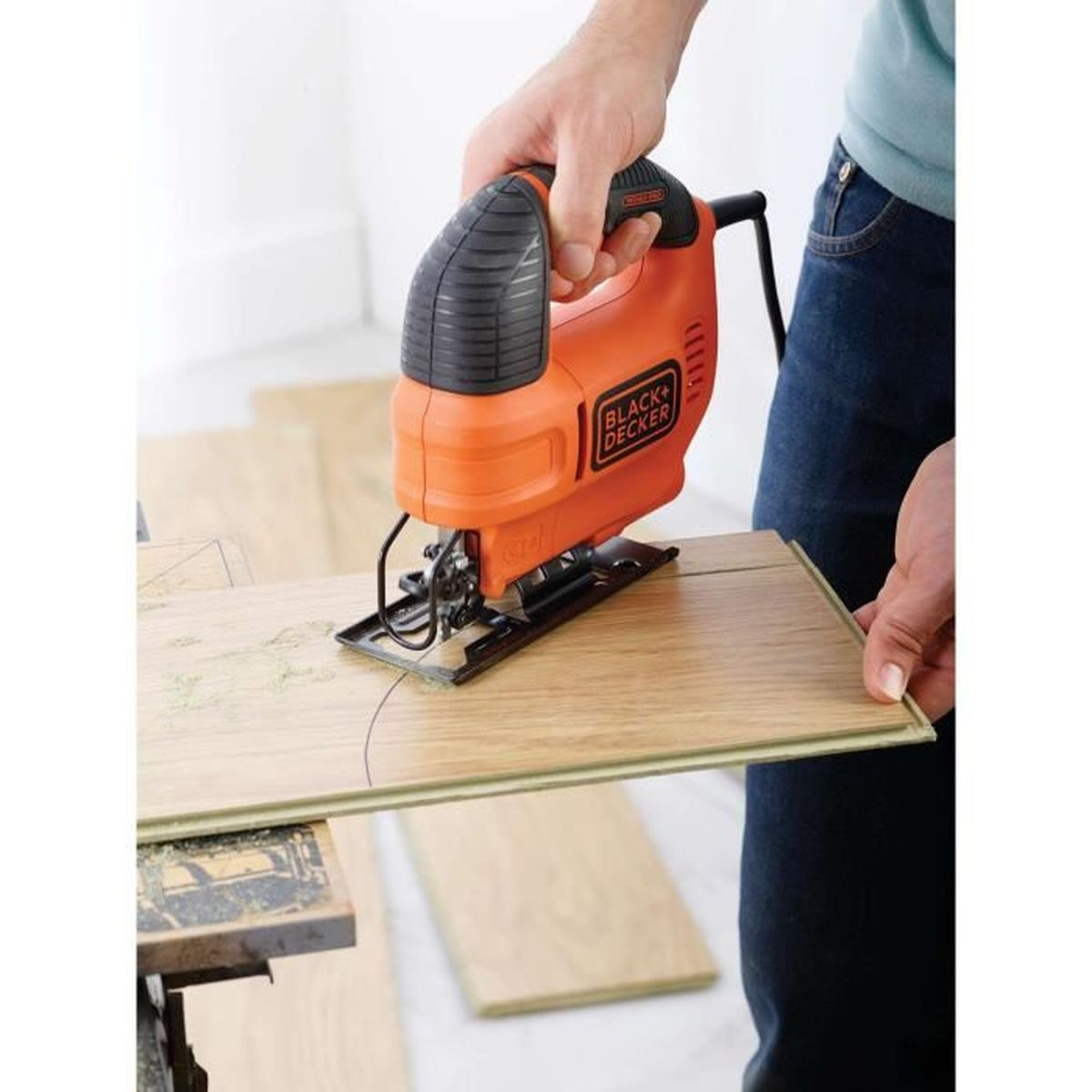 Een persoon gebruikt een oranje decoupeerzaag om houten planken te snijden.