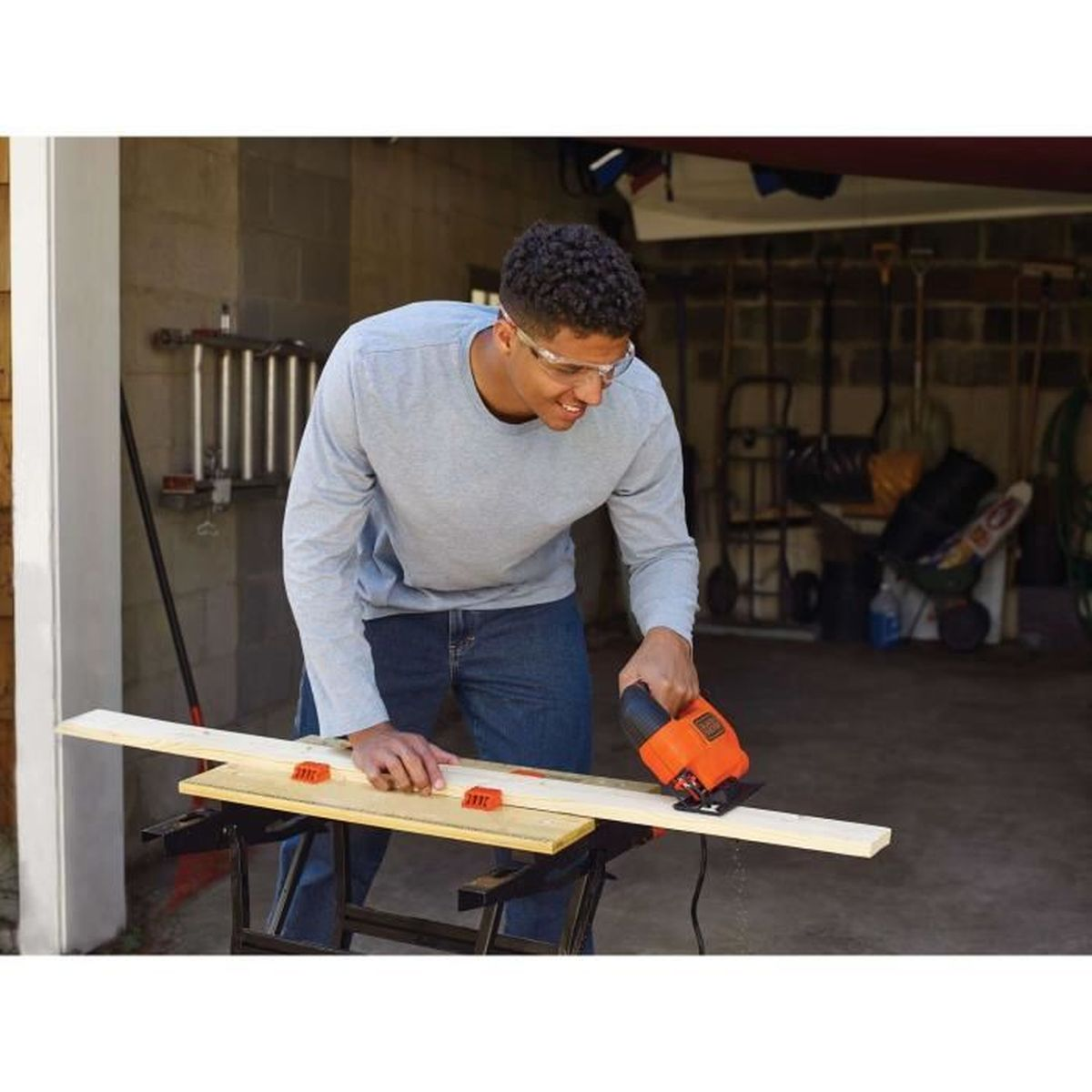 Man met veiligheidsbril zaagt met decoupeerzaag een houten plank.