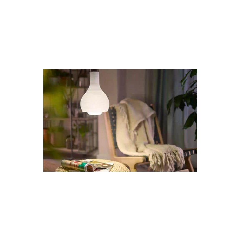 Una lampada a sospensione pende sopra una sedia con una coperta. Riviste su uno sgabello.