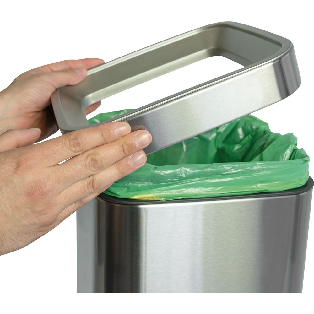 Person öffnet den Deckel eines silbernen Mülleimers mit grünem Müllbeutel.