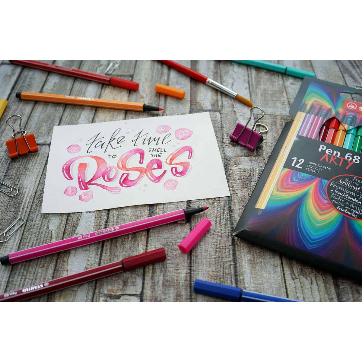 Buntstifte auf Holzoberfläche mit Kalligraphie-Karte und Stiftepackung.