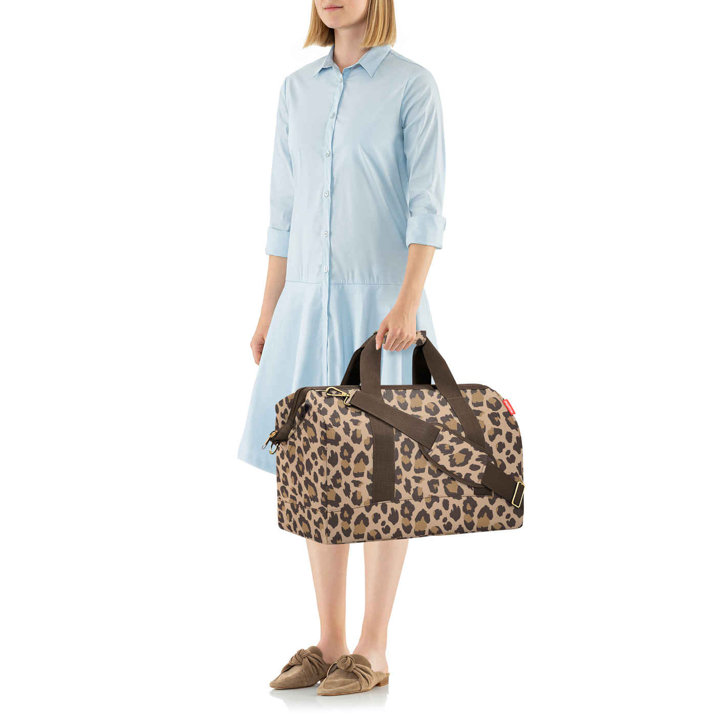 Eine Frau in einem hellblauen Kleid hält eine Dufflebag mit Leopardenmuster.