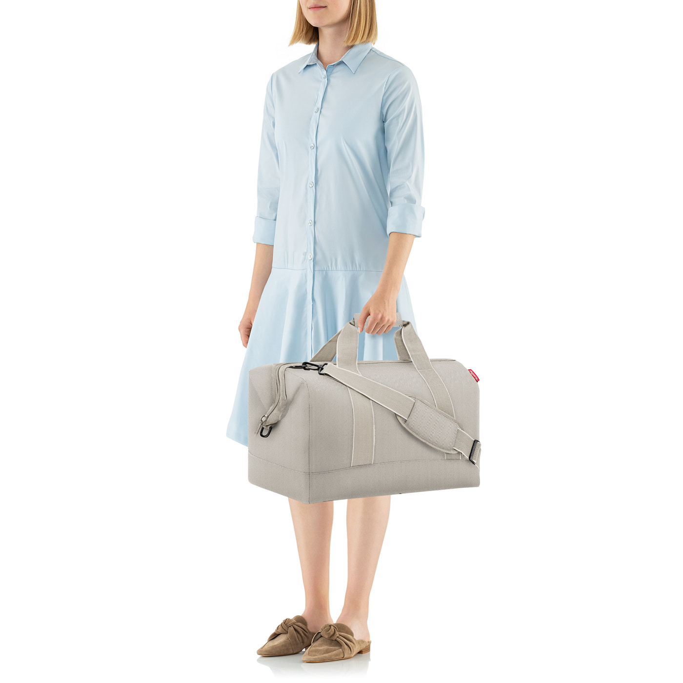 Eine Frau in hellblauem Kleid trägt eine graue Reisetasche.