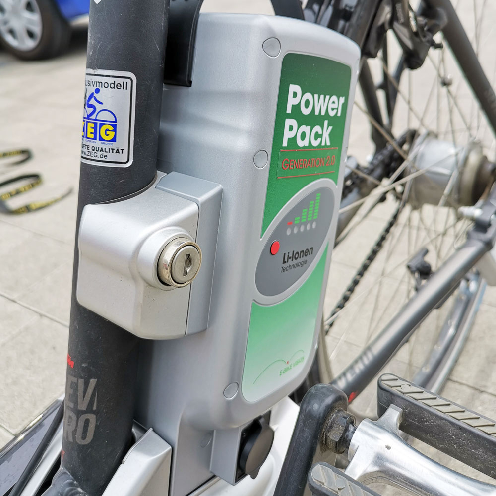 Silberne E-Bike-Akkupack mit 'Power Pack Generation 2.0'-Etikett, Schloss und Pedalen.