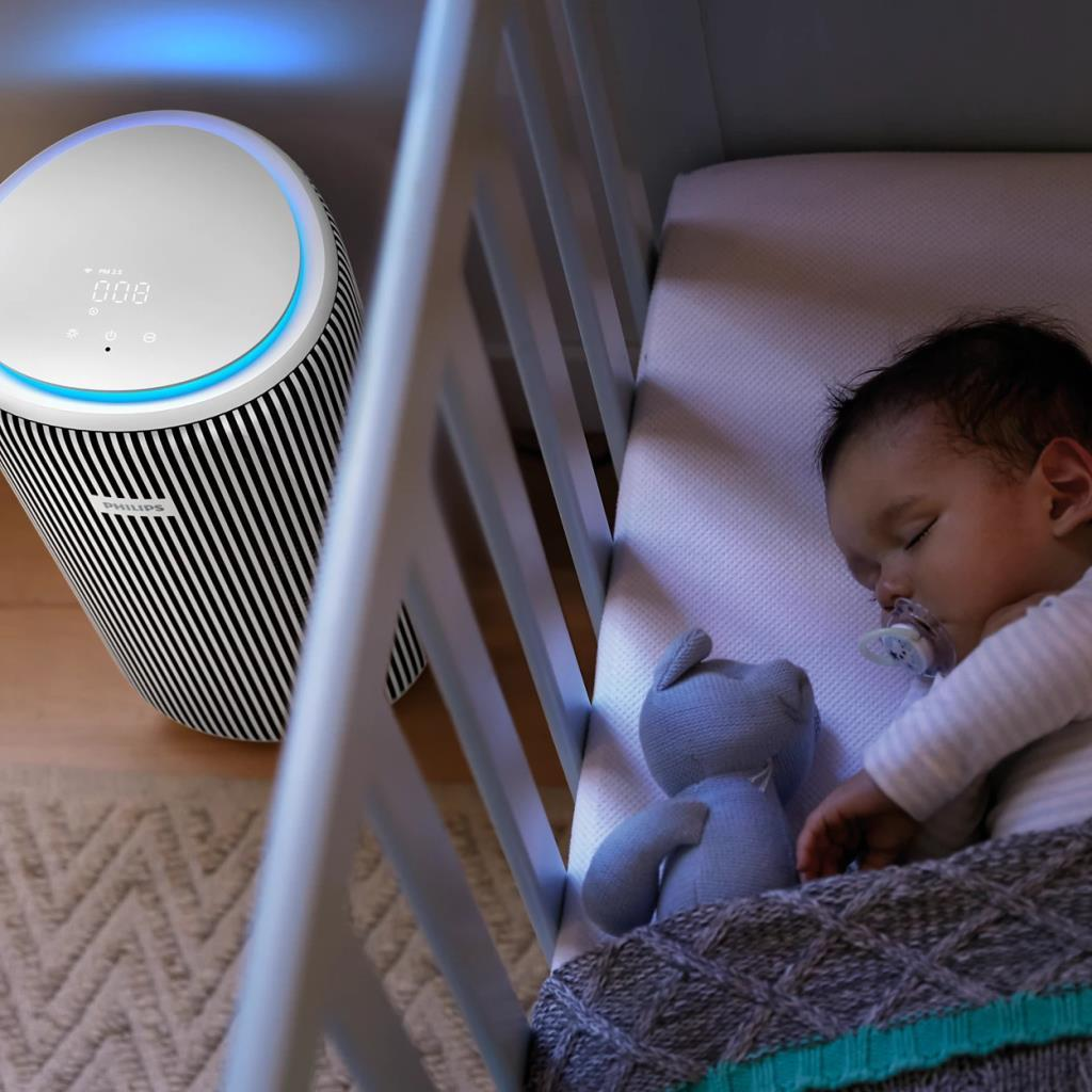 Ein Baby schläft in einem Kinderbett neben einem Luftreiniger mit blauem Licht.