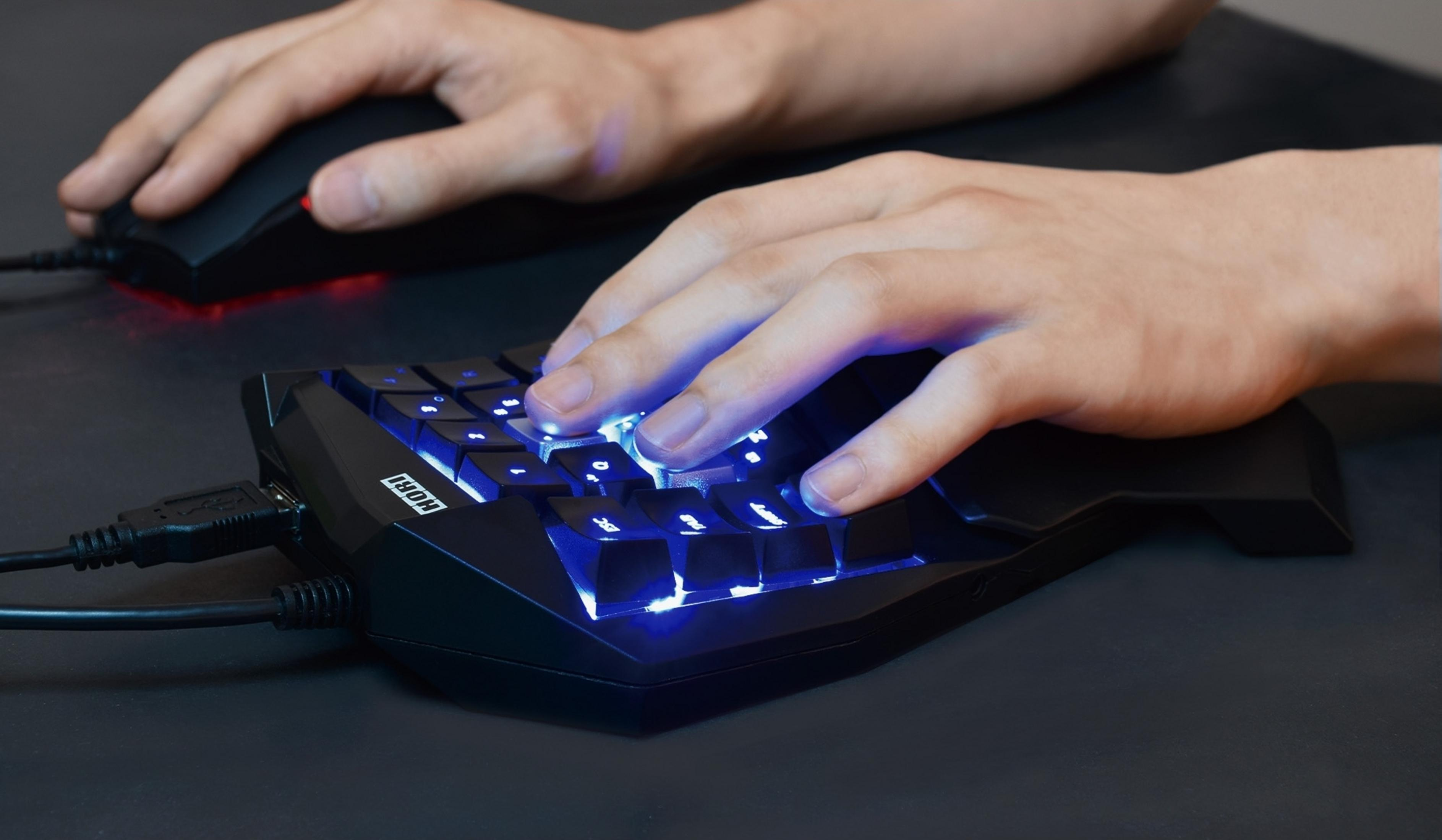 Mani su una tastiera gaming nera con retroilluminazione blu e un mouse.