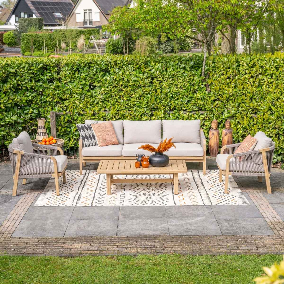 Een tuinloungeset met bank, fauteuils, salontafel en vloerkleed voor een haag.