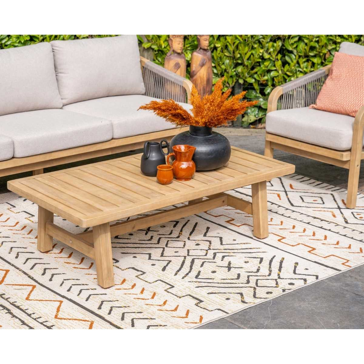 Houten salontafel met vazen en gedroogde bloemen, naast bank, fauteuil en patroonkleed.