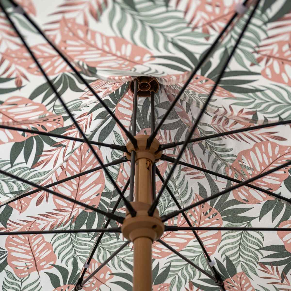 Close-up van een paraplu met roze en groen bladpatroon. Metalen baleinen zijn zichtbaar.