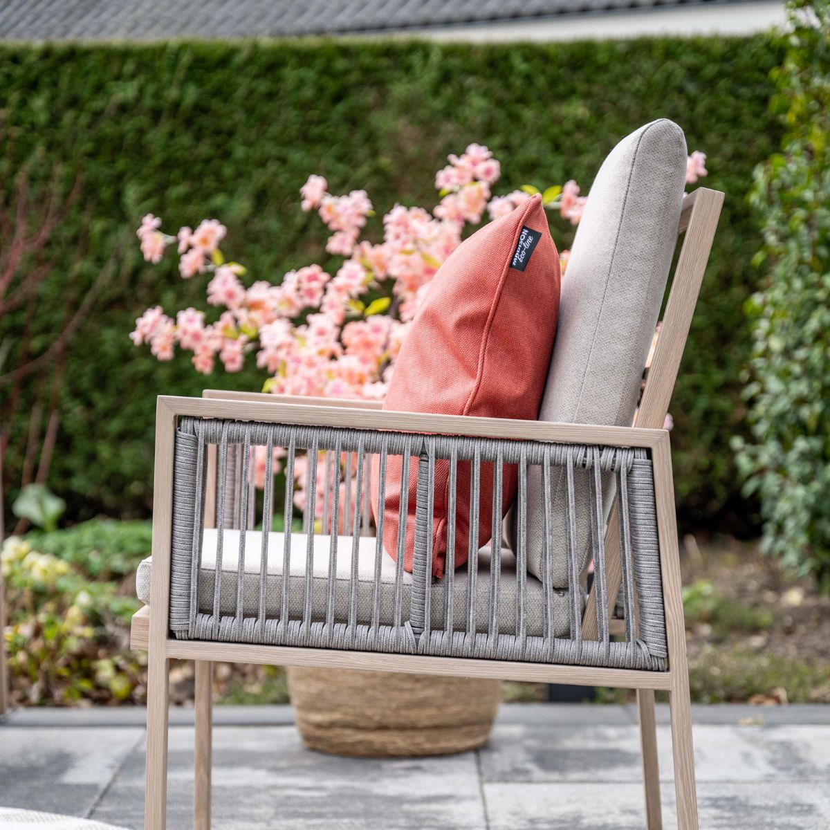 Houten en touw tuinstoel met kussens, tegen een bloeiende achtergrond.