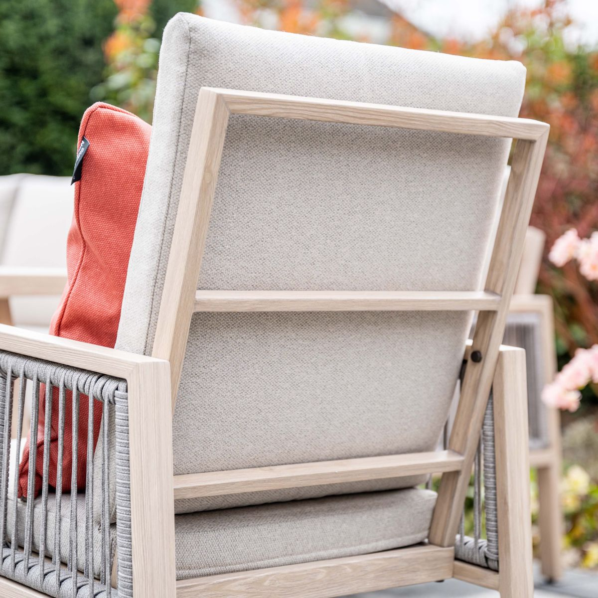 Grijze fauteuil met geweven zijkanten en een oranje kussen buiten.