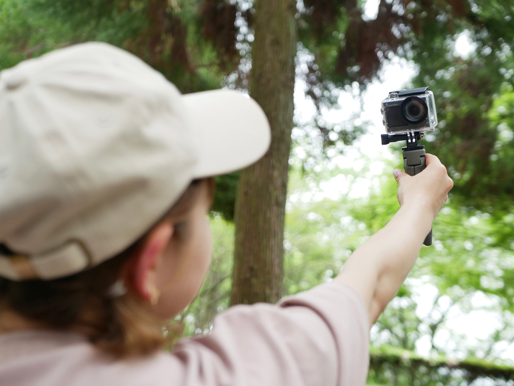 Person mit Kappe hält Action-Kamera in einem Wald