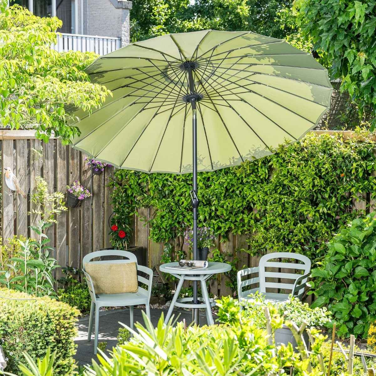 Een tuintafel met twee stoelen onder een parasol, omgeven door groen.