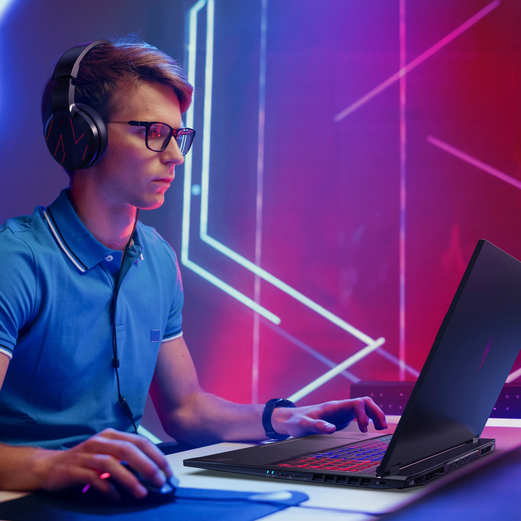Ein Mann mit Kopfhörern spielt an einem Laptop mit farbiger Tastaturbeleuchtung.