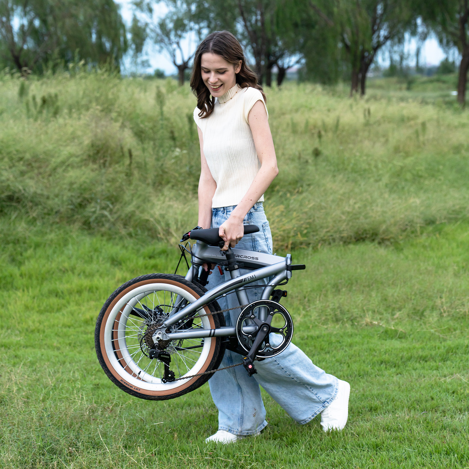 Eine Frau mit einem faltbaren Fahrrad im Freien auf grünem Gras.