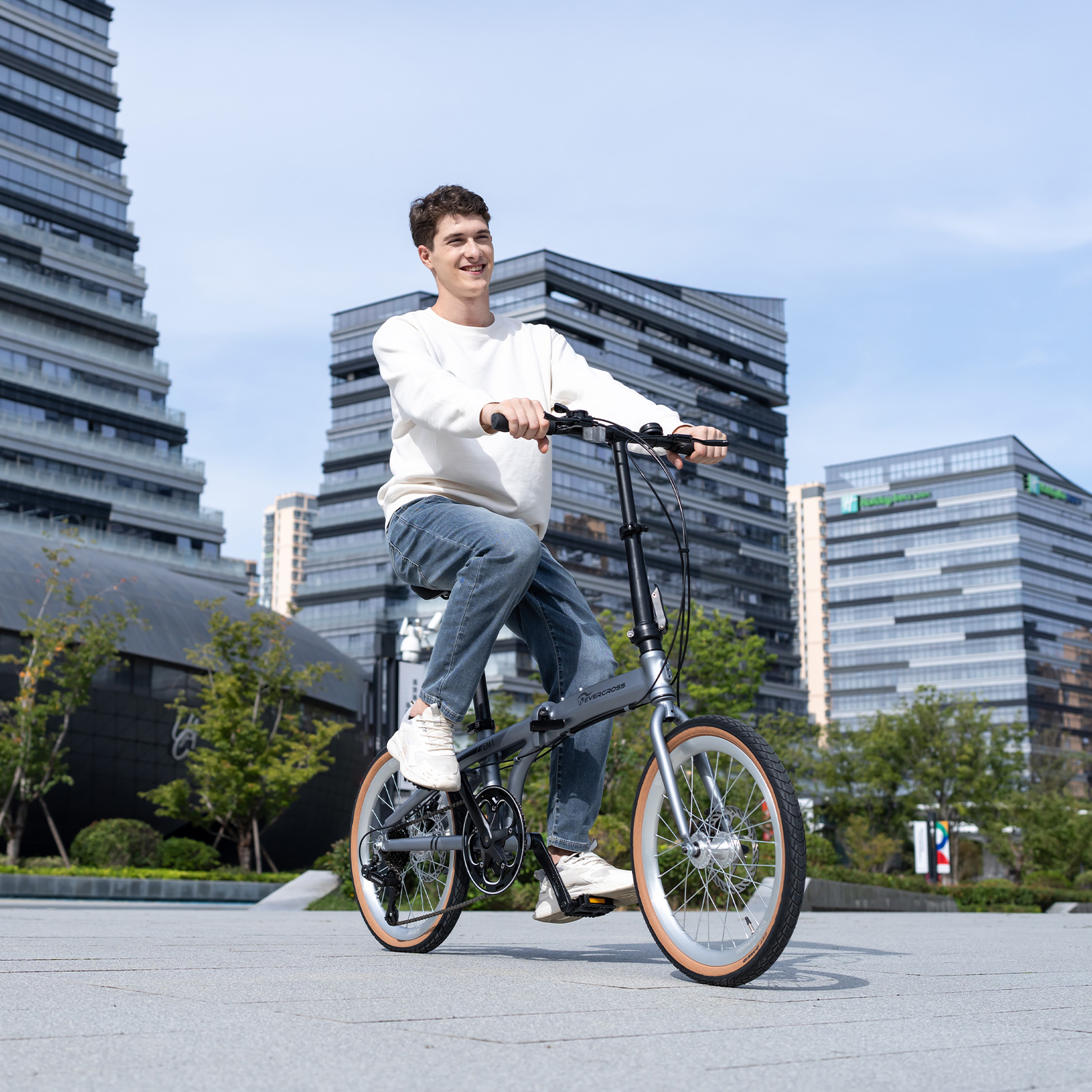 Ein Mann fährt ein graues Klapprad in der Nähe moderner Gebäude.