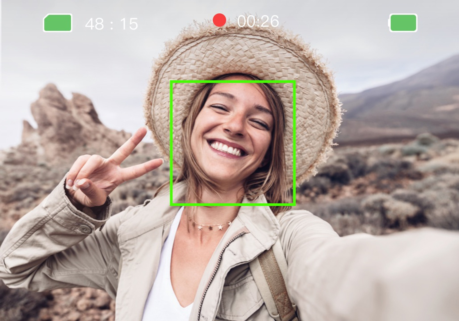 Frau mit Hut macht Selfie, V-Geste, im Hintergrund felsige Landschaft.