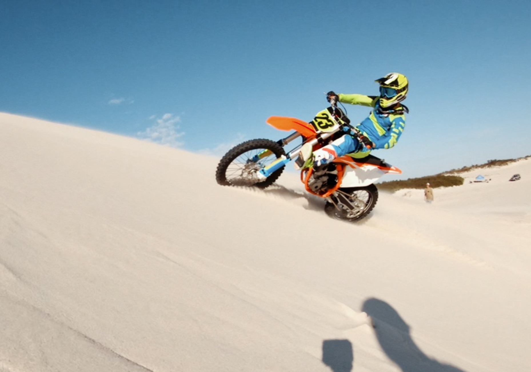 Ein Motorradfahrer fährt einen Sandhügel hinauf, blauer Himmel.
