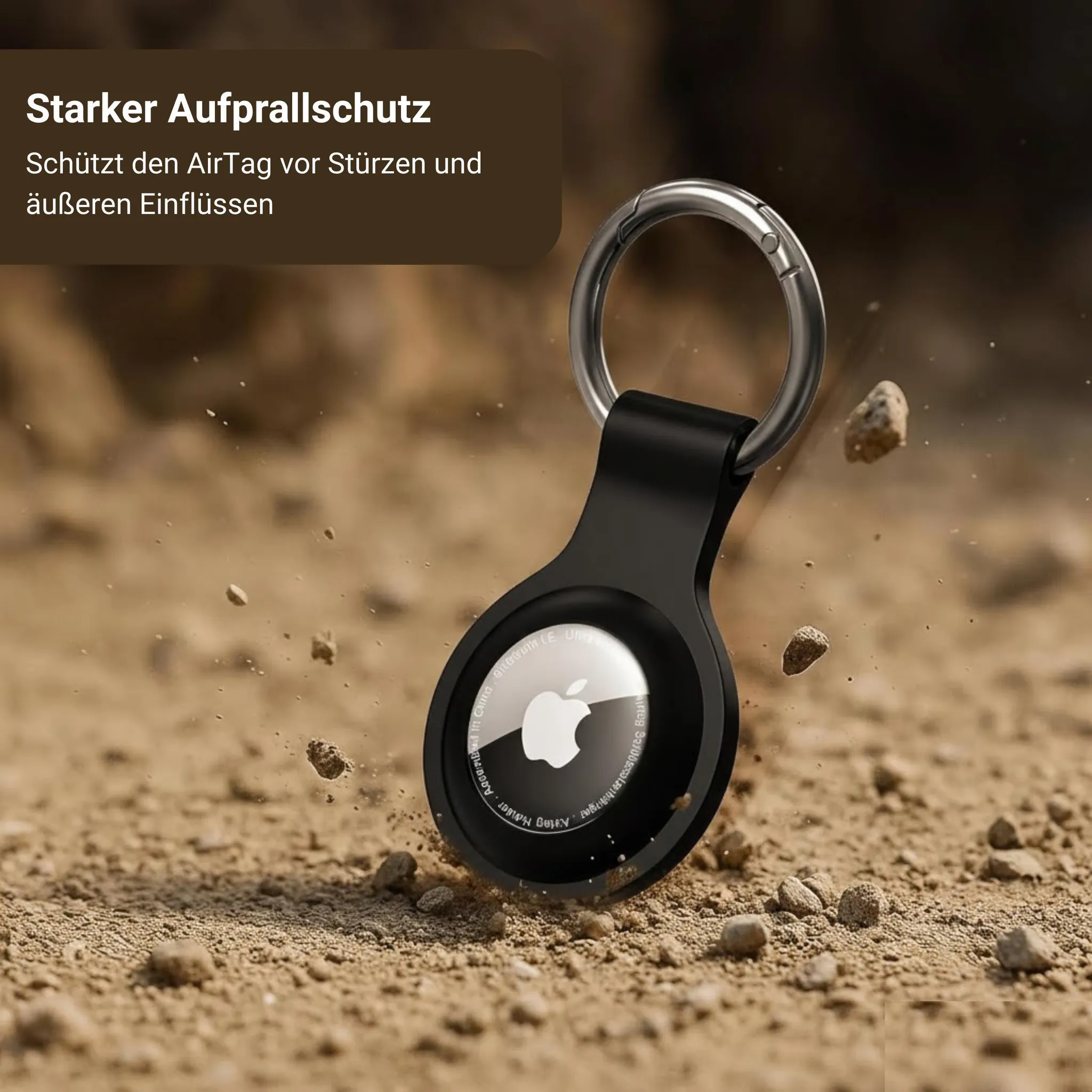 Schwarzer AirTag-Halter mit Schlüsselring fällt auf staubigem Boden.