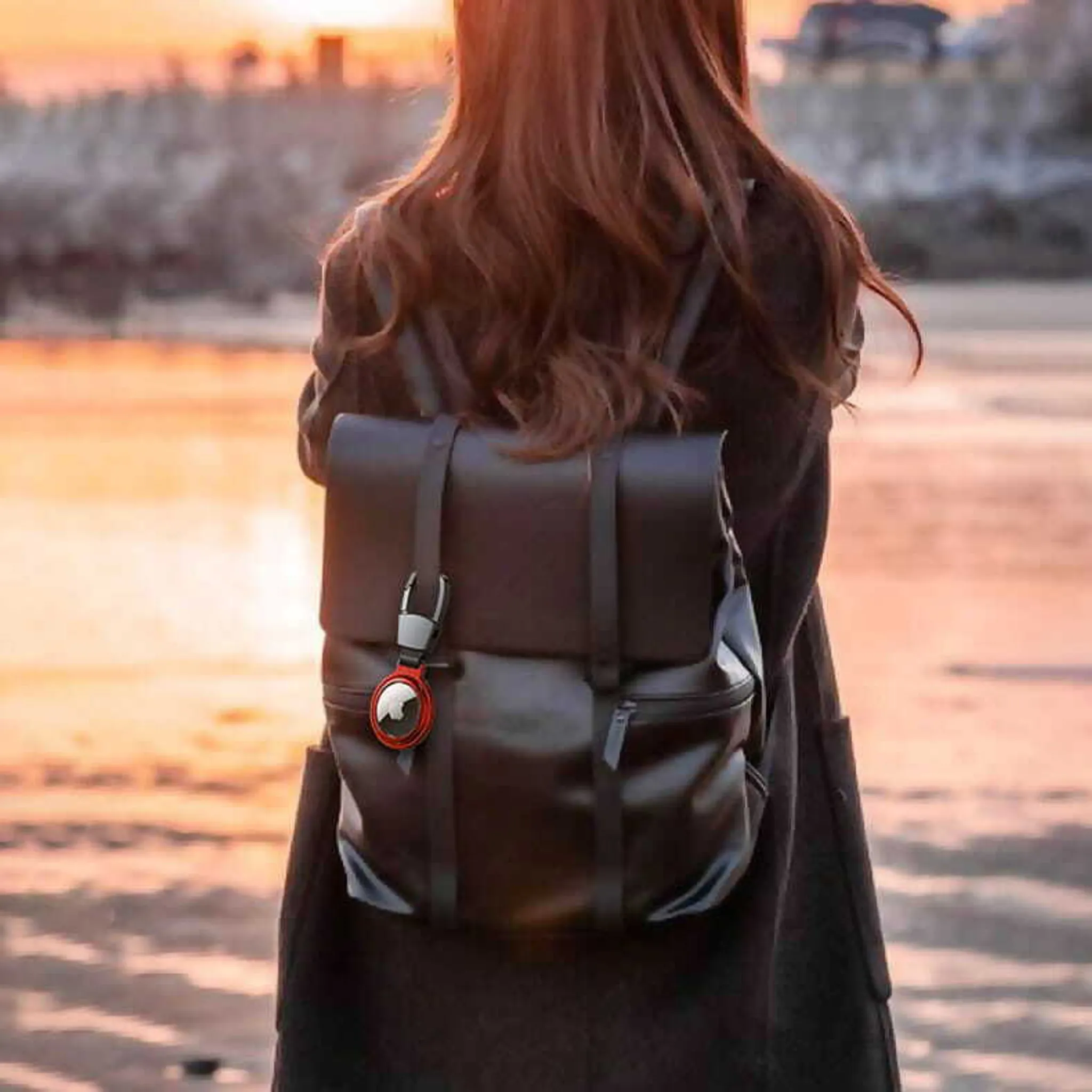 Eine Person mit braunen Haaren trägt einen schwarzen Rucksack mit einem roten Schlüsselanhänger.