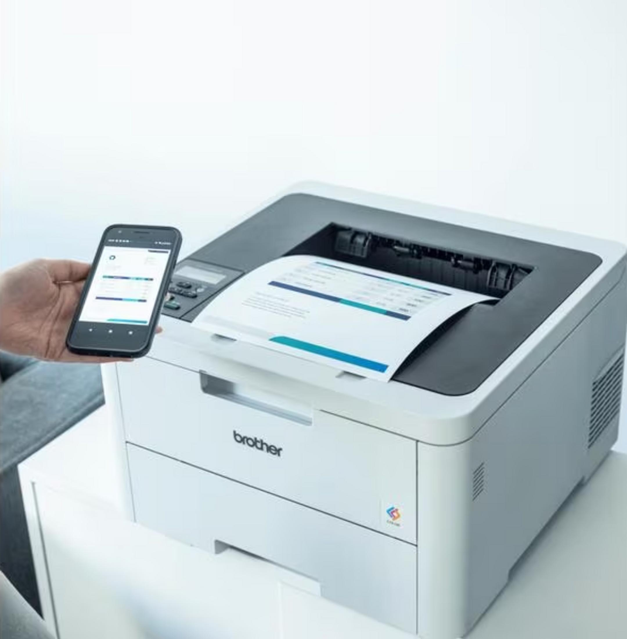 Eine Hand hält ein Smartphone mit Diagrammen neben einem Brother-Drucker mit Dokument.