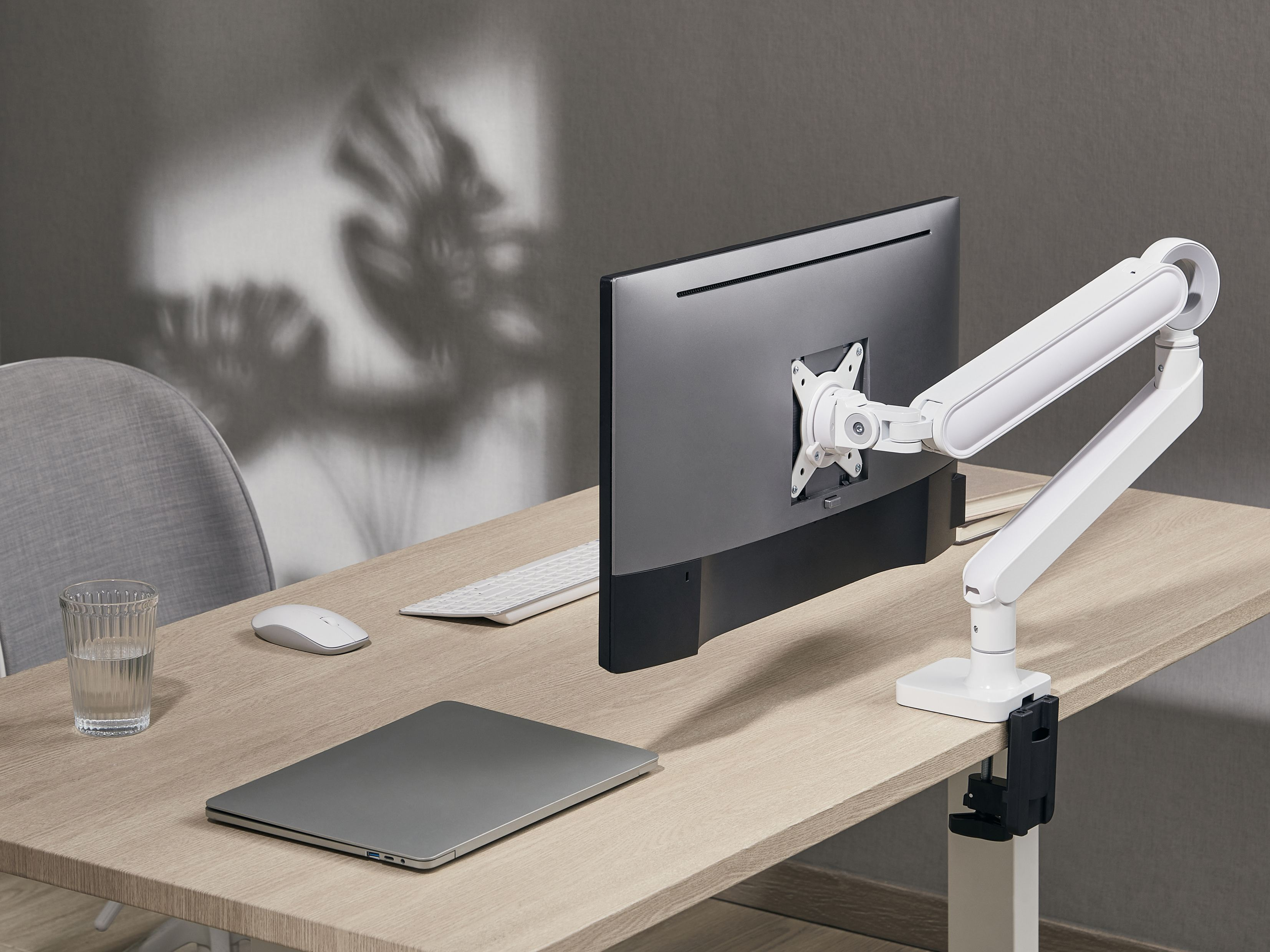 Ein Schreibtisch mit einem Laptop, einer Maus, einer Tastatur, einem Glas Wasser und einem Monitorarm.