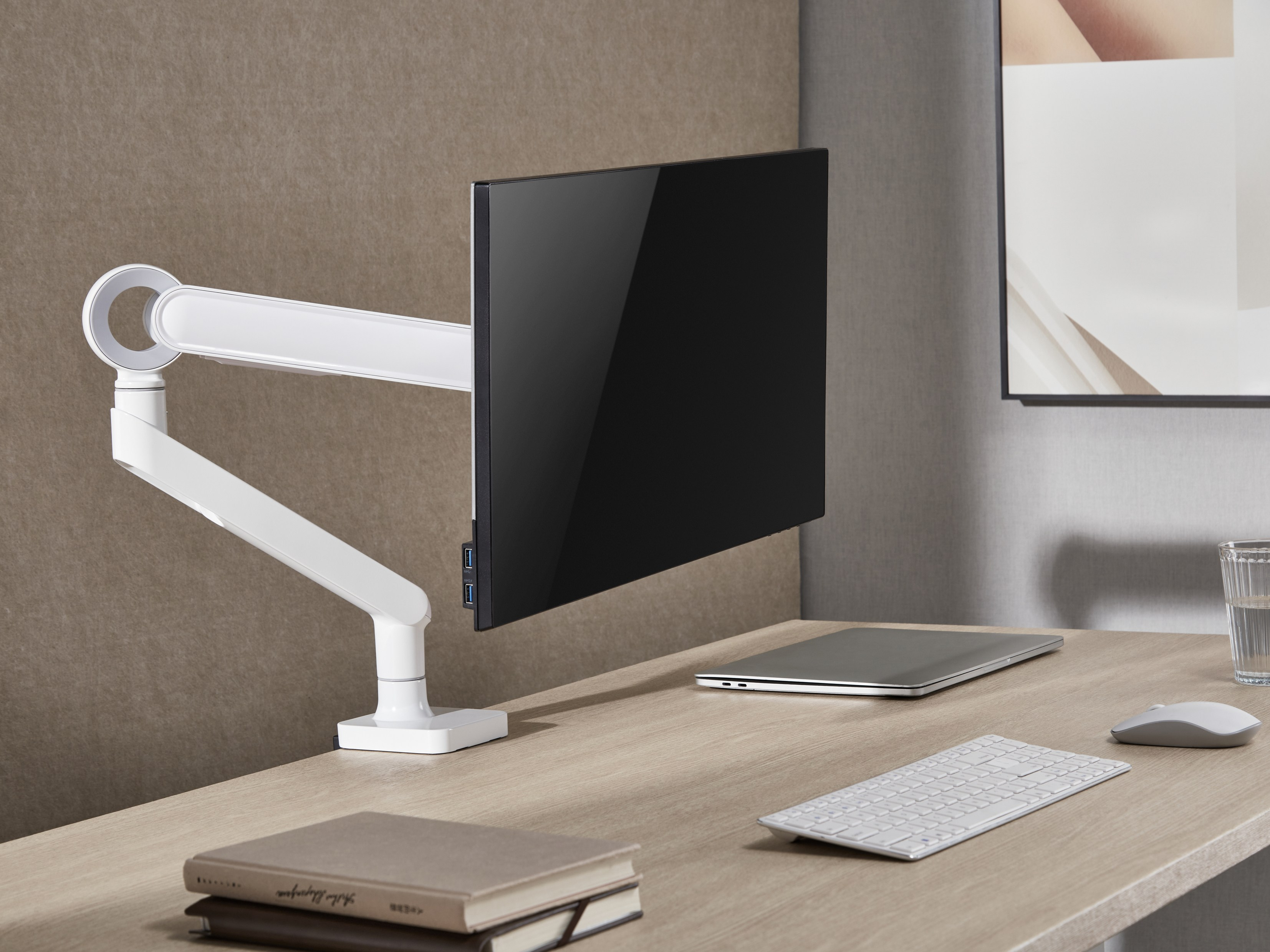 Moderner Schreibtisch mit Monitorarm, Laptop, Tastatur, Maus und Glas Wasser.
