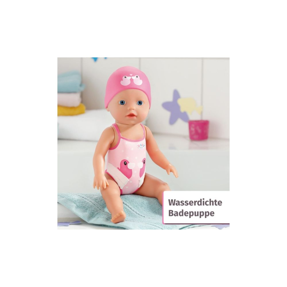 Eine puppe in einem pinken badeanzug mit entenmotiv sitzt auf einem hellblauen handtuch.