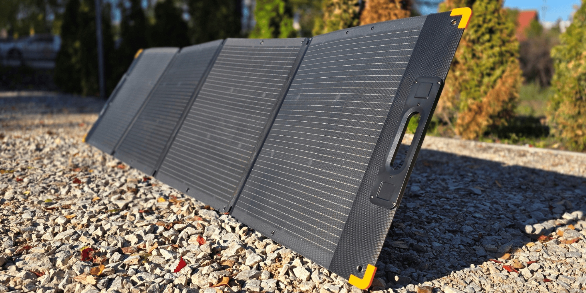 Składany, czarny panel słoneczny z żółtymi akcentami leży na żwirze.