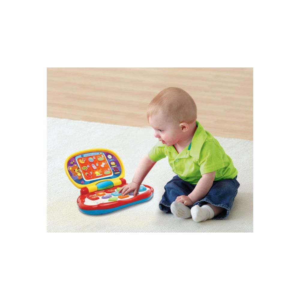 Ein Baby spielt mit einem bunten Spielzeuglaptop auf einem Teppich.