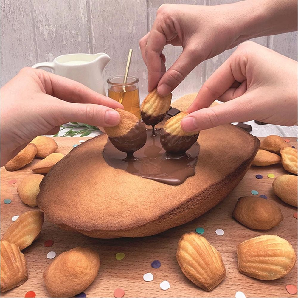 Hände tauchen Madeleines in flüssige Schokolade auf einem großen Kuchen.