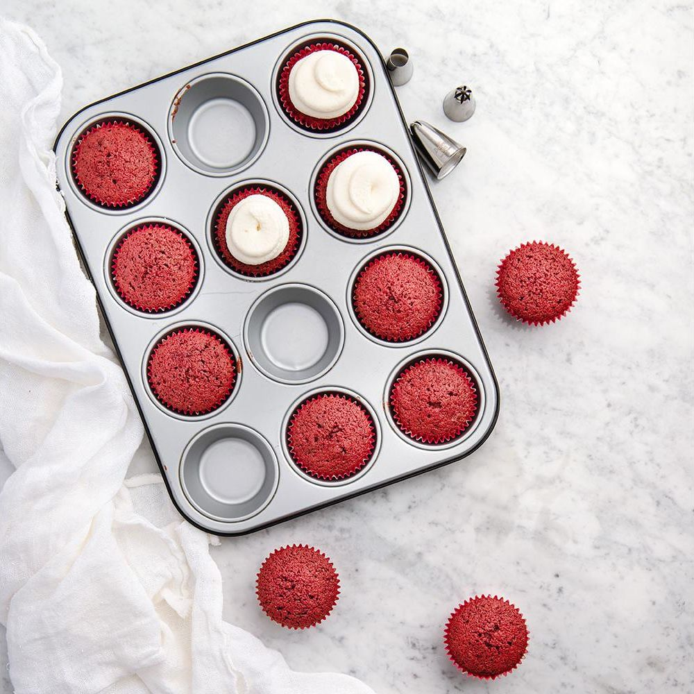 Rote Samt-Cupcakes in einer Muffinform, einige mit Zuckerguss, mit Spritztüllen.