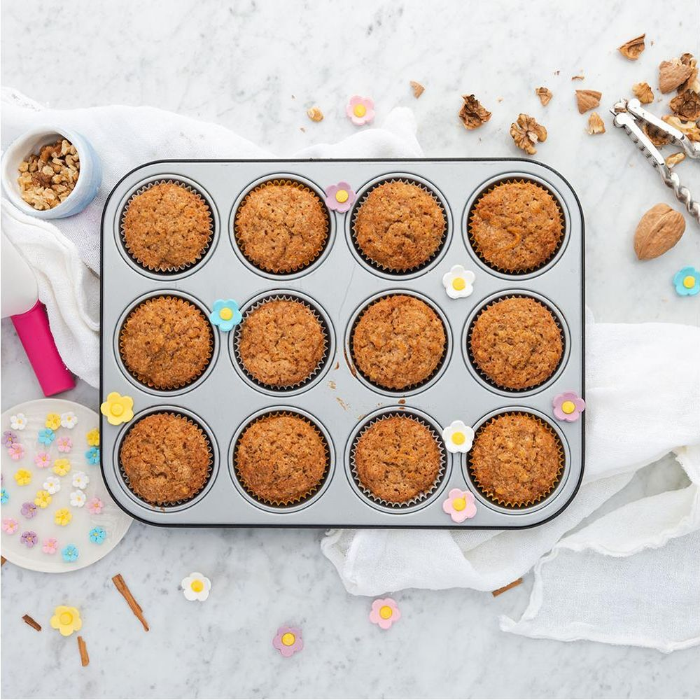 Ein Dutzend goldbraune Muffins in einer Muffin-Form, mit Walnüssen und bunten Blumen.