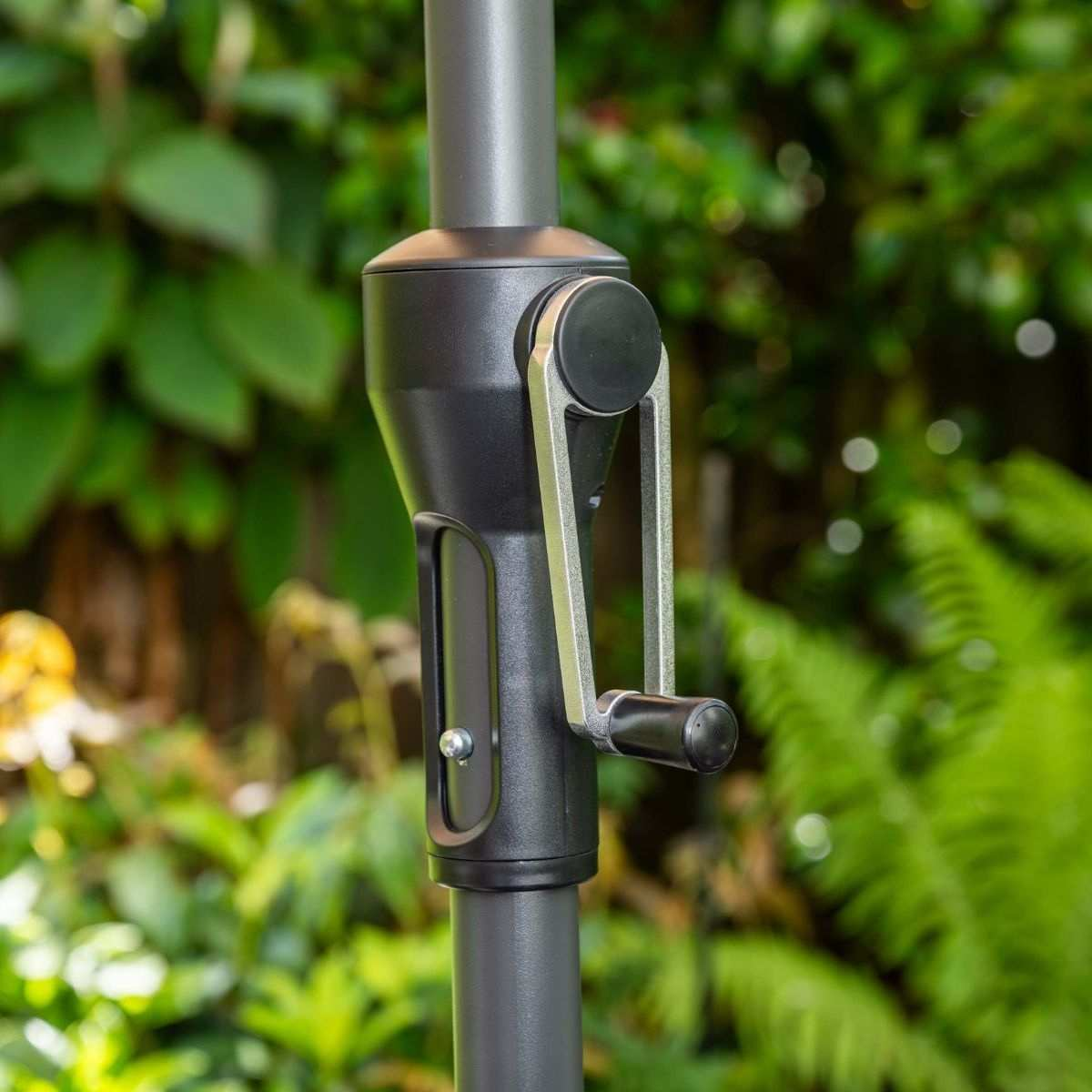 Een grijze paraplupaal met een slinger mechanisme tegen groen gebladerte.