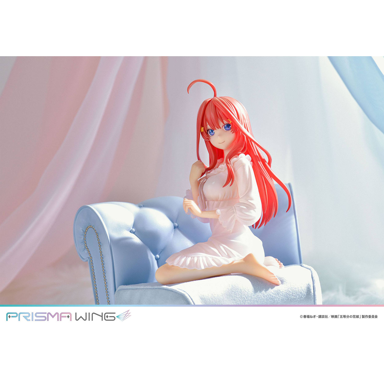 Eine Anime-Figur mit roten Haaren sitzt auf einer blauen Couch, mit zarten Stoffen im Hintergrund.