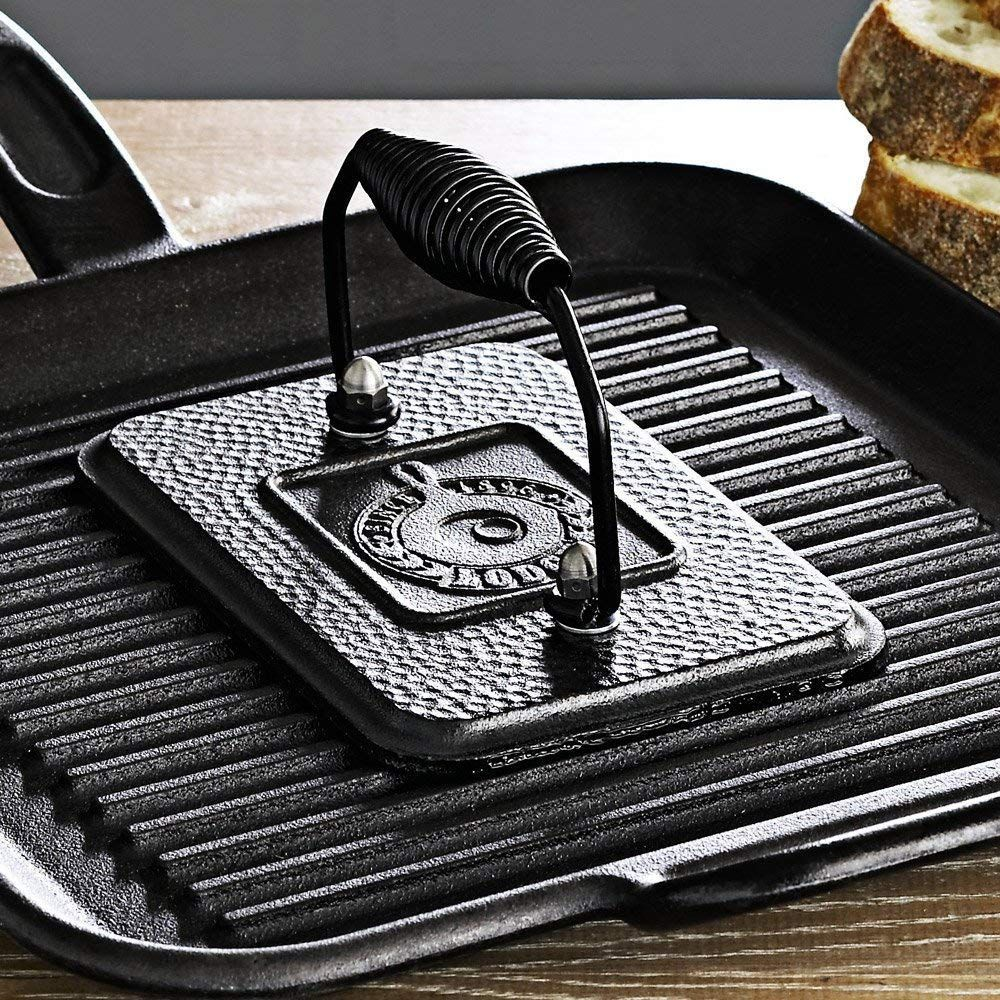 Padella grill in ghisa con pressa e fette di pane sullo sfondo.